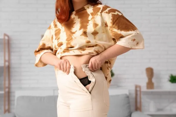 Image of woman trying to do her trousers up after pregnancy weight gain Selly Oak