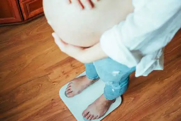 Image of woman weighing herself and experiencing weight gain through pregnancy Selly Oak